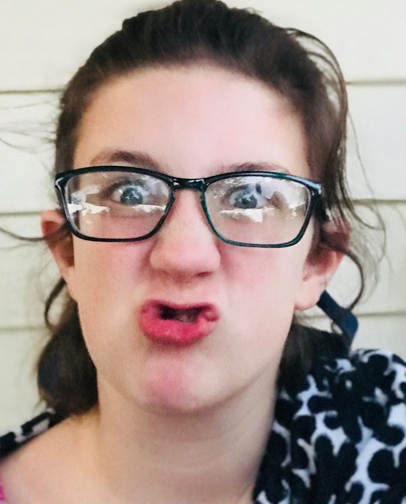 A 12 year old girl in glasses makes a goofy face at the camera.