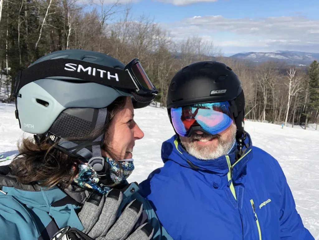 A man and woman in ski gear smile at each other.